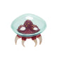 A small Metroid figure with a translucent aqua dome, a dark red textured body, and four curved cream-colored claws, shown on a plain white background.