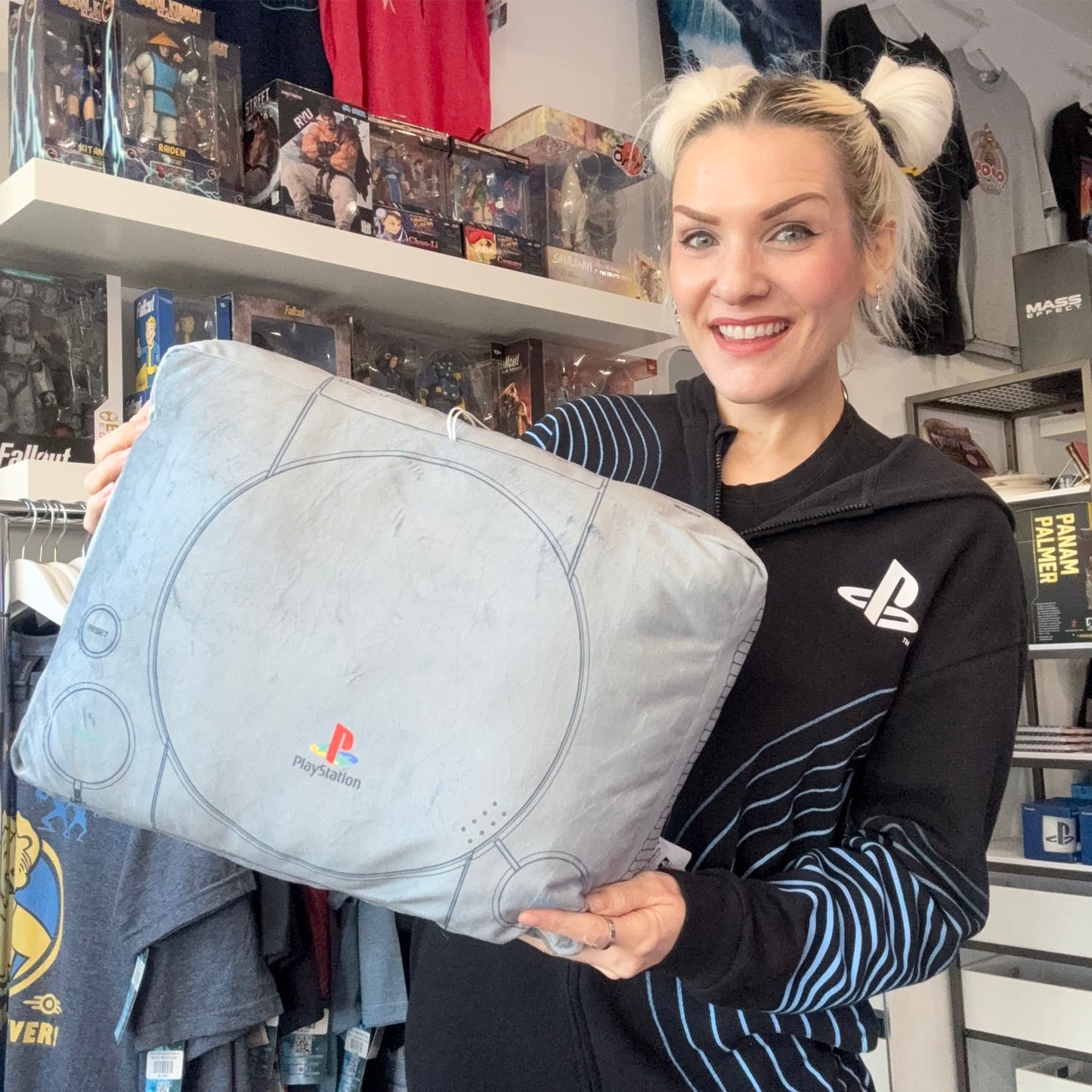 Blonde woman holding a PlayStation console shaped pillow.