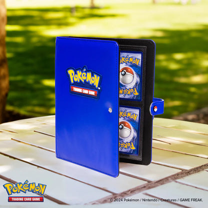 A blue Pokémon 4-pocket snap binder with Pokémon cards visible in the pockets, placed on a wooden table outdoors.