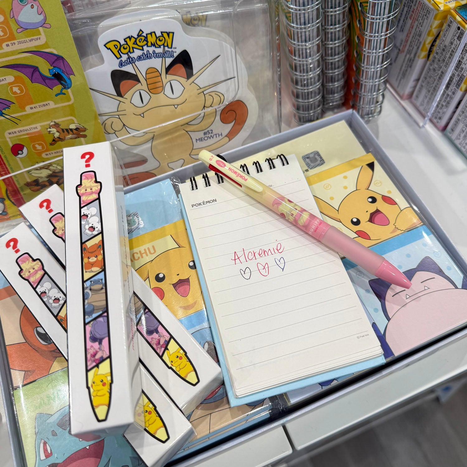 Notepad with the Pokémon name Alcremie written on it with Alcremie pen laying beside it. 