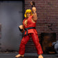 Street Fighter Ken action figure posed in a fighting stance, wearing a red gi with a black belt and brown finger wraps, set against a brick wall and barrel backdrop.