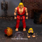 Street Fighter Ken 1/6 scale action figure with red gi, black belt, yellow hair, and interchangeable heads, displayed with accessories on a dark tabletop against a brick wall backdrop.