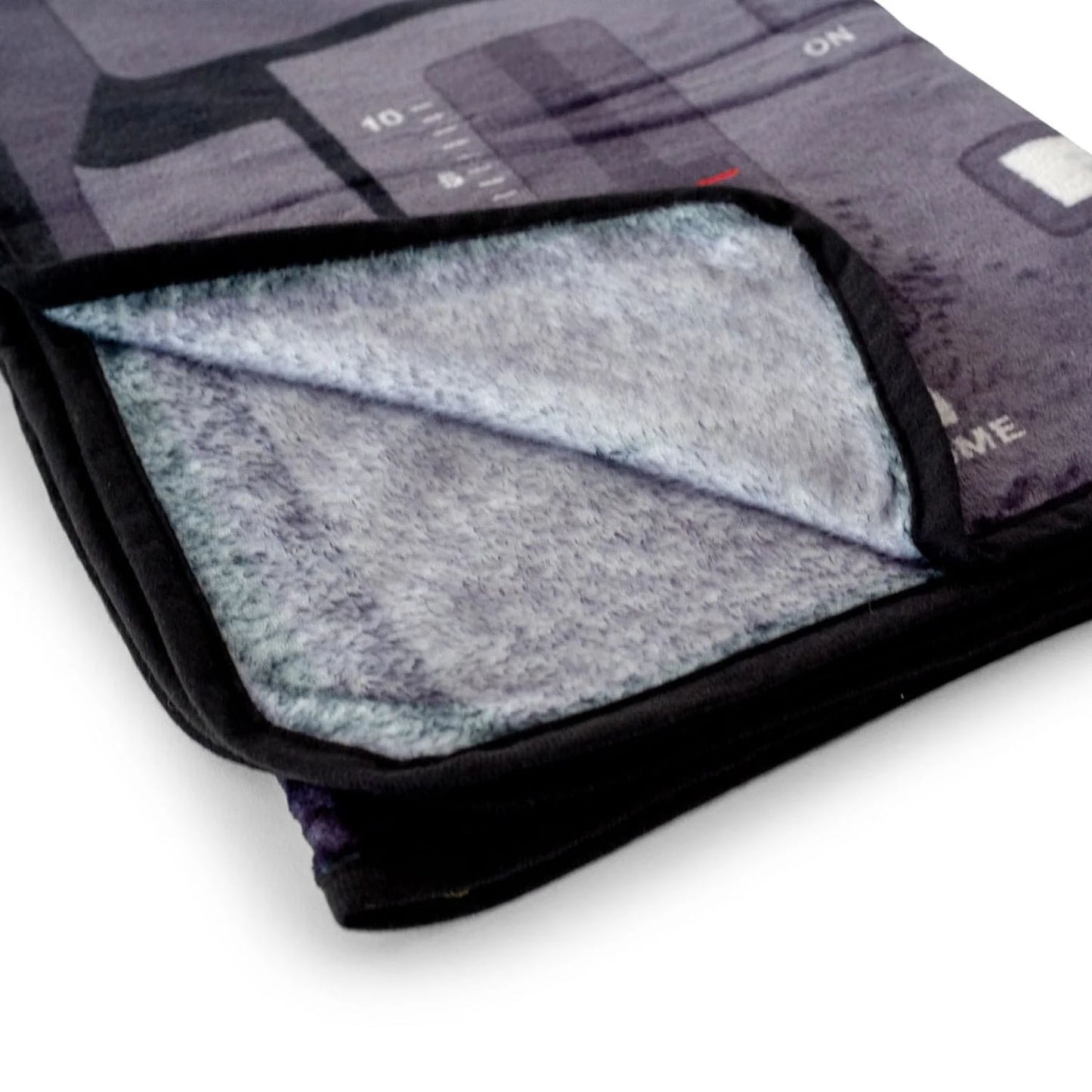 A folded blanket with a dark gray and black futuristic cityscape print, showing a soft gray sherpa fleece lining on a white background.