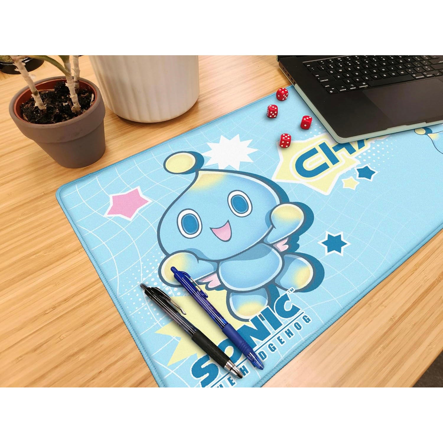 Desk setup with a Chao character mouse pad, pens, and dice on a wooden desk.